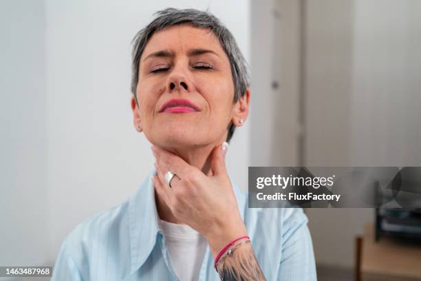 woman touching her sore throat, while making a grimace because of the pain - throat pain stock pictures, royalty-free photos & images