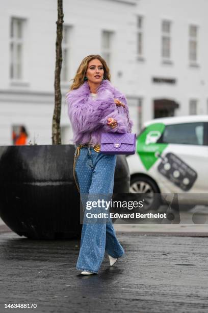 Emili Sindlev wears blue earrings, a pale purple large fluffy fur jacket, a white t-shirt, a purple shiny leather quilted Timeless handbag from...