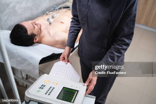 female nurse analysed patient's cardiogram, while he lay on the examination table during an ecg procedure - electrode stock pictures, royalty-free photos & images
