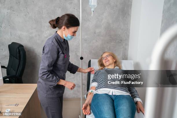 female nurse checking on a female patient while she receiving iv drip - iv infusion stockfoto's en -beelden