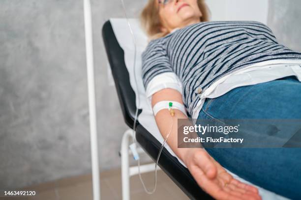 paciente do sexo feminino irreconhecível recebendo gotejamento intravenoso, enquanto deitada na mesa de exame - infused - fotografias e filmes do acervo