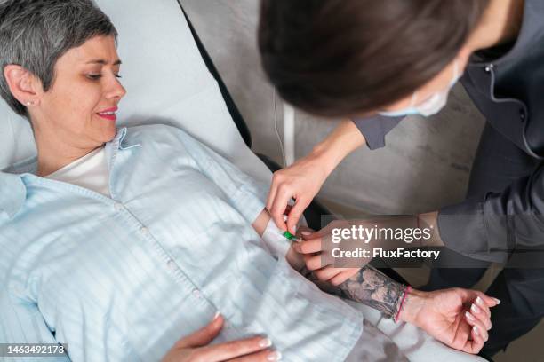 高齢女性患者の点滴を調整する女性看護師 - 生理食塩水 ストックフォトと画像