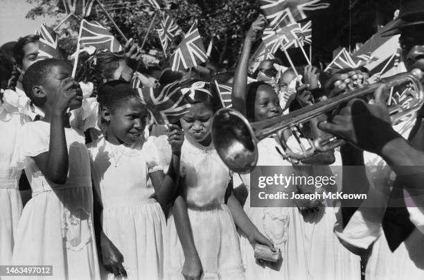 Crowd of schoolgirls waving Union Jack flags wait to welcome Princess Margaret during her visit to Trinidad. They all wear formal white dresses and a...