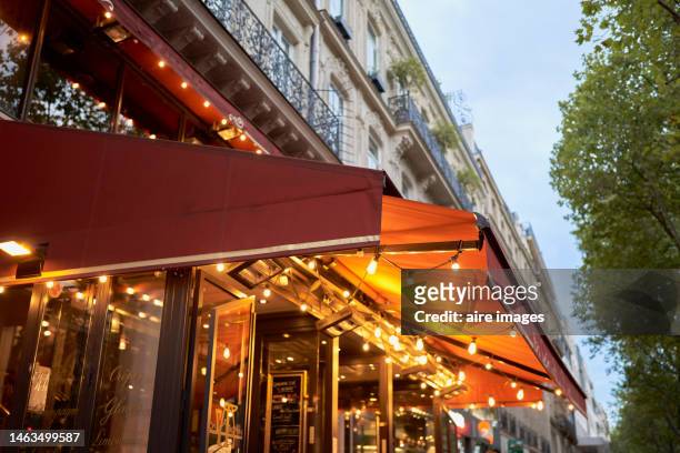 facade of a cafeteria with a red awning decorated with lights, on the upper part there are apartments with balconies and in one there is a flower pot. - awning stock pictures, royalty-free photos & images
