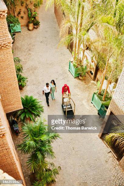 Wide overhead shot of bellman helping guests in hotel courtyard