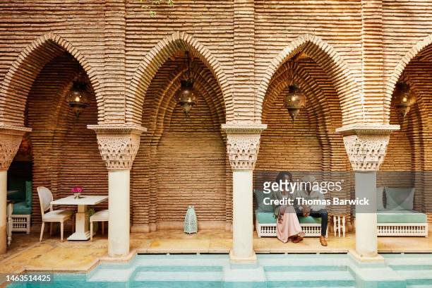 wide shot of couple holding hands while sitting in courtyard of luxury hotel - marrakech morocco stock pictures, royalty-free photos & images