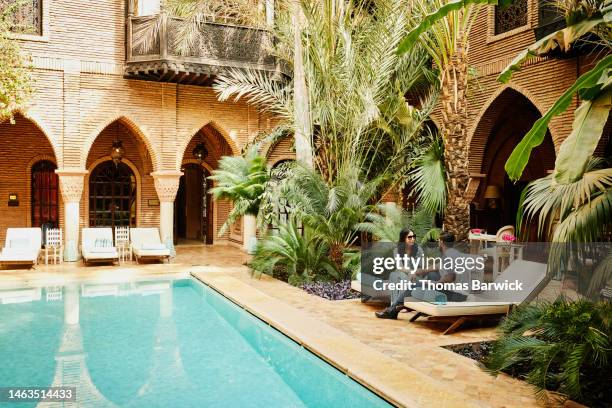 wide shot of couple sitting by pool in courtyard of luxury hotel - luxushotel stock-fotos und bilder