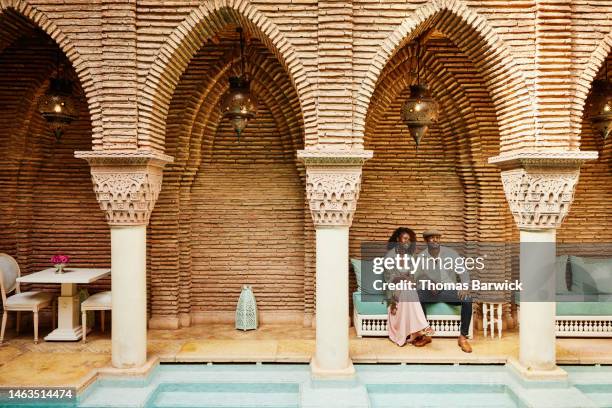 wide shot of couple holding hands while sitting in courtyard of luxury hotel - north africa stockfoto's en -beelden