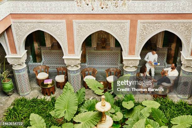 Wide shot of couple being served tea in courtyard of luxury hotel