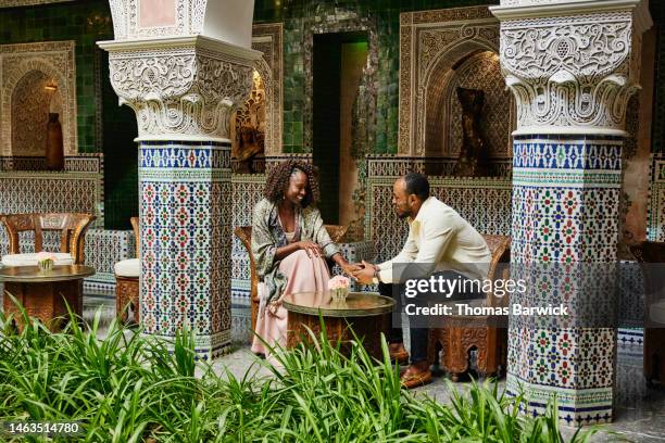 wide shot of smiling couple relaxing in courtyard of luxury hotel - true luxury stock-fotos und bilder