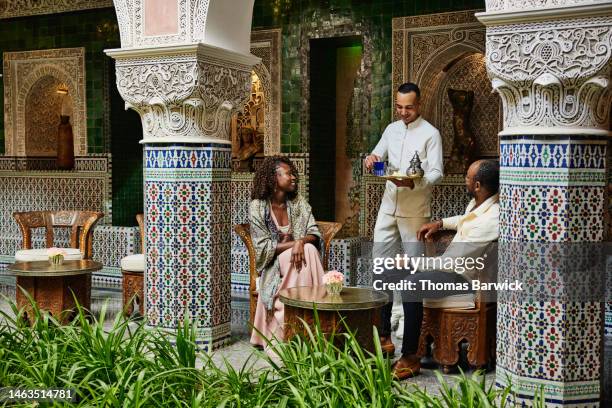 wide shot of couple being served tea in courtyard of luxury hotel - luxury destinations stockfoto's en -beelden