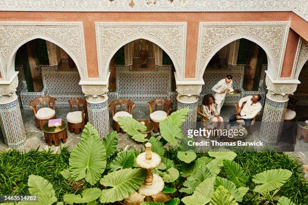 wide shot of couple being served tea in courtyard of luxury hotel - morocco stock pictures, royalty-free photos & images