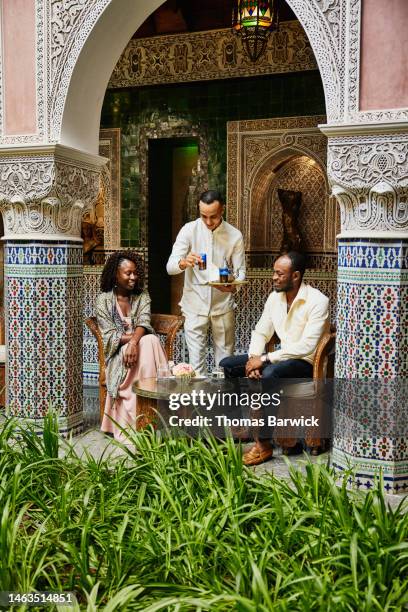 wide shot of couple being served tea in courtyard of luxury hotel - turismo responsable fotografías e imágenes de stock