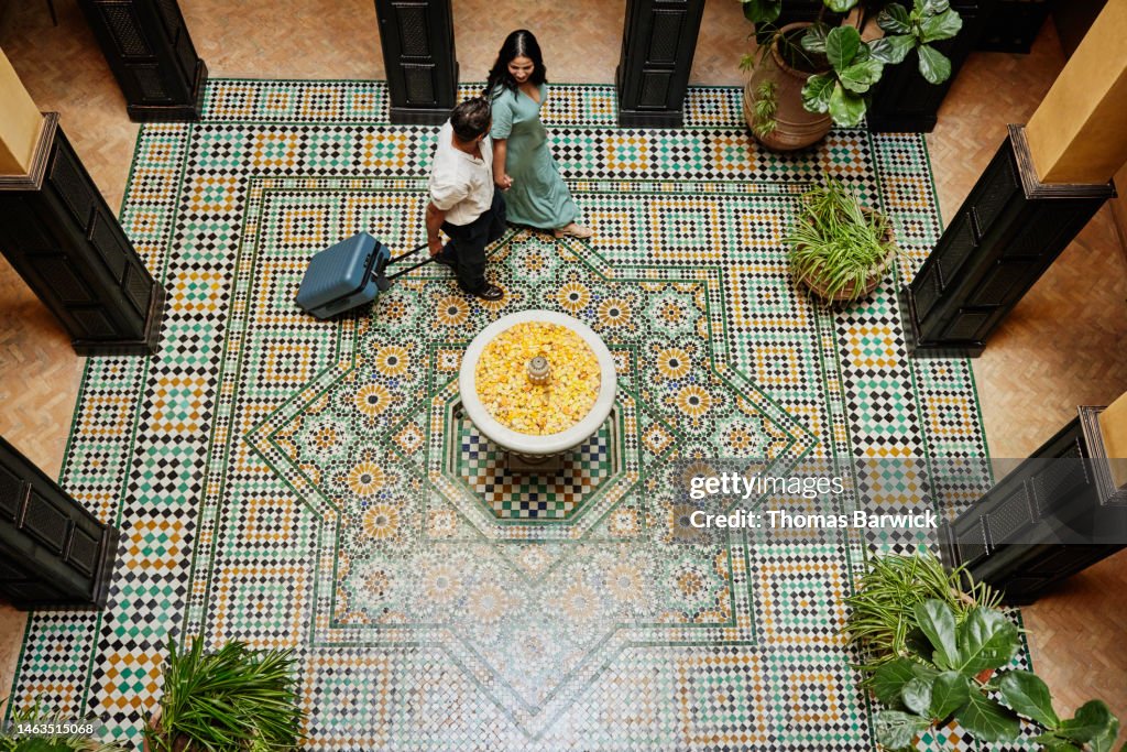 Wide shot of couple walking across colorfully tiled floor of hotel