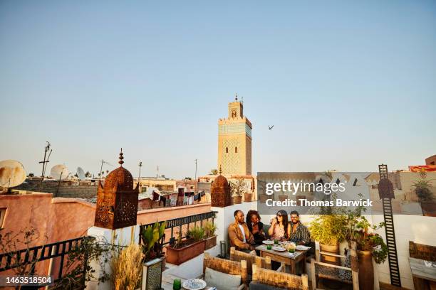 wide shot of smiling friends dining at rooftop restaurant in marrakech - rooftop dining foto e immagini stock