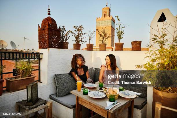 wide shot of smiling friends dining at rooftop restaurant in marrakech - affluent dining stock-fotos und bilder