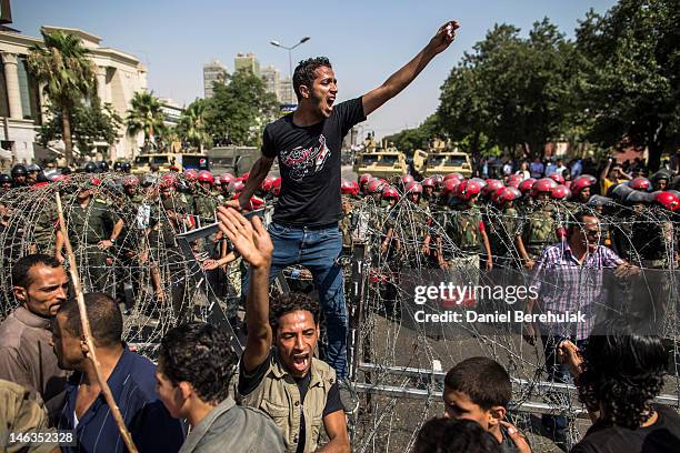 Protestor stands on a barricade of barbed wire as Egyptian military police stand guard during a protest against presidential candidate Ahmed Shafiq...