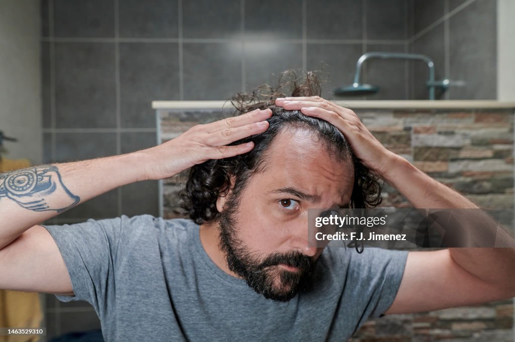 Man looking at his hair in bathroom mirror