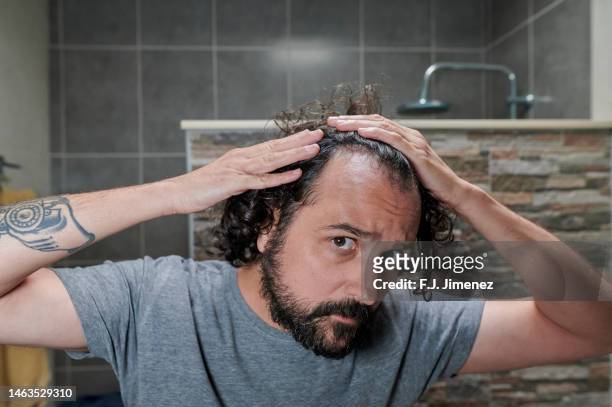 man looking at his hair in bathroom mirror - haaruitval stockfoto's en -beelden