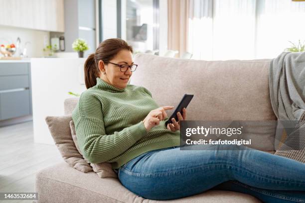 mujer sonriente relajada sentada en el sofá usando el teléfono - casa real española fotografías e imágenes de stock