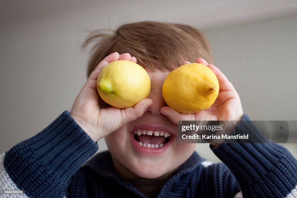 Boy holding two lemons in his eyes