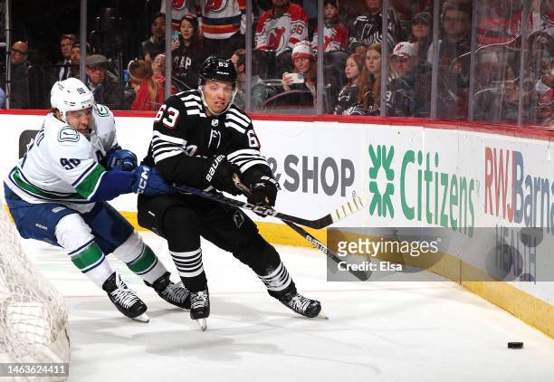 Jesper Bratt of the New Jersey Devils wraps around the net as Andrei Kuzmenko of the Vancouver Canucks defends in overtime at Prudential Center on...