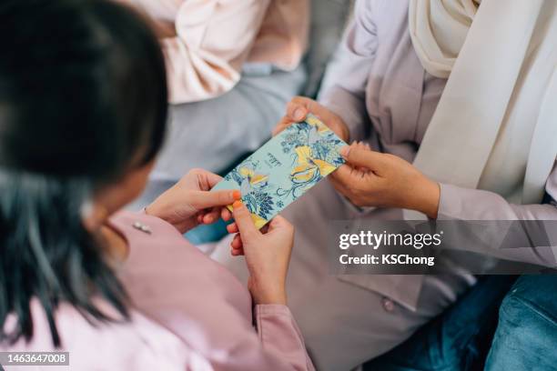hari raya malaiische muslimische familie in traditioneller tracht erhält ein geldpaket auf hari ray feier im wohnzimmer. - hari raya celebration stock-fotos und bilder