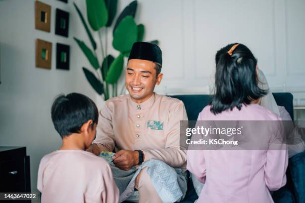 hari raya malay muslim family in traditional costume receives a money packet on hari ray celebration in living room . - shared prosperity stock pictures, royalty-free photos & images