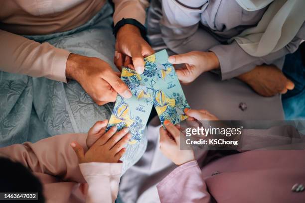 hari raya malaiische muslimische familie in traditioneller tracht erhält ein geldpaket auf hari ray feier im wohnzimmer. - hari raya celebration stock-fotos und bilder