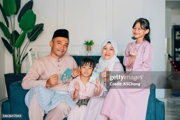 hari raya malaiische muslimische familie in traditioneller tracht mit green pocket auf hari ray feier im wohnzimmer. - hari raya celebration stock-fotos und bilder