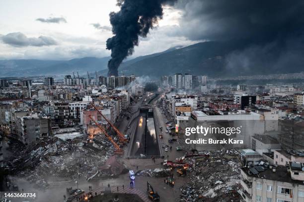 Smoke billows from the Iskenderun Port as rescue workers work at the scene of a collapsed building on February 07, 2023 in Iskenderun, Turkey. A...