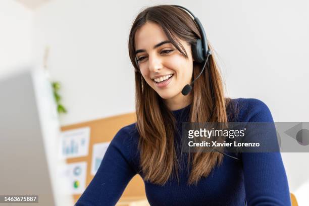 young pretty woman with a headset working online on computer sitting at desk in office workplace. millennial female working in call center talking with customer. - empleada administrativa stock-fotos und bilder
