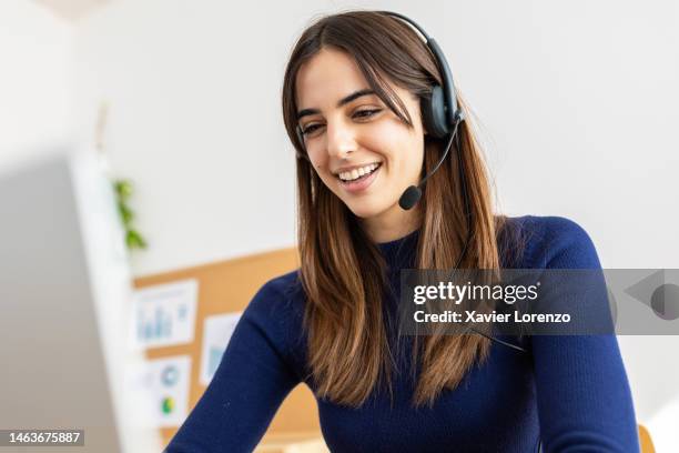 young pretty woman with a headset working online on computer sitting at desk in office workplace. millennial female working in call center talking with customer. - oficio de comunicaciones fotografías e imágenes de stock