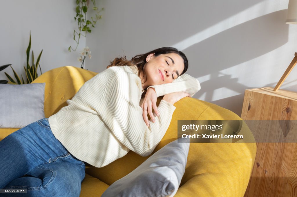 Young beautiful woman enjoying sunlight resting on sofa at home. Simple living concept