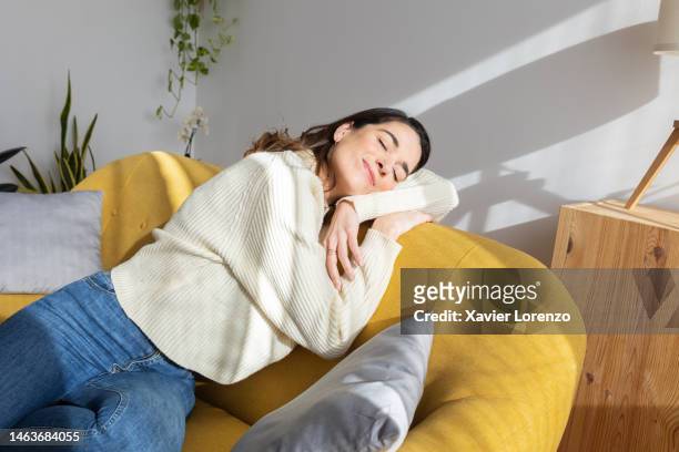 young beautiful woman enjoying sunlight resting on sofa at home. simple living concept - calm woman stockfoto's en -beelden