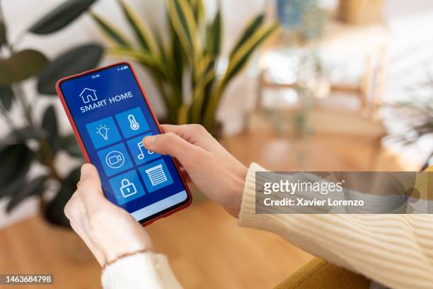 close up cropped young adult woman holding smartphone using iot smart home app while resting on sofa. new trends, technology and domestic lifestyle concept - erwachsener über 30 stock-fotos und bilder
