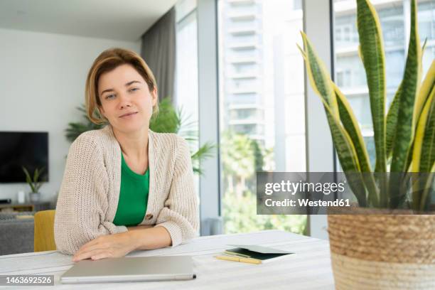 woman sitting with laptop and note pad on desk at home - portrait frau arabisch frontal stock-fotos und bilder