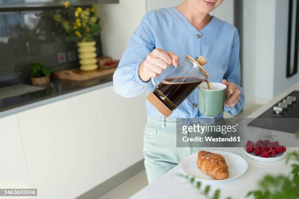 woman pouring coffee in cup with croissant on counter at home - coffee plunger stock pictures, royalty-free photos & images