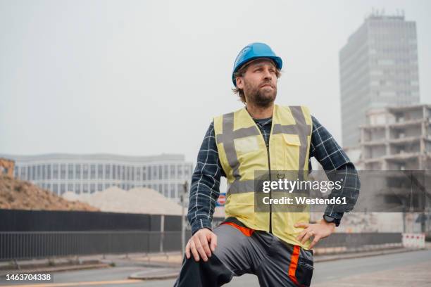 contemplative mature blue-collar worker standing in front of construction site - laborer stock-fotos und bilder