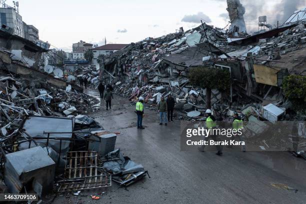 People walk past collapsed buildings on February 07, 2023 in Iskenderun, Turkey. A 7.8-magnitude earthquake hit near Gaziantep, Turkey, in the early...