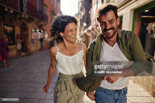 playful couple having fun while running on the street. - travel destinations running stock pictures, royalty-free photos & images