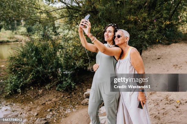 smiling women taking selfie using smart phone at park - age contrast stock pictures, royalty-free photos & images