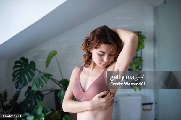 young woman looking at armpit in bathroom - sostén fotografías e imágenes de stock
