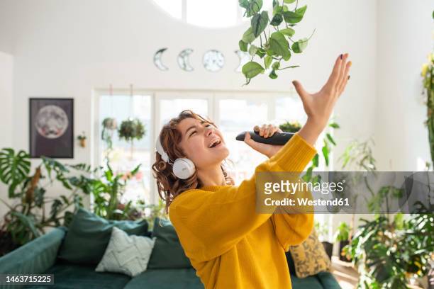smiling young woman singing in living room at home - karaoke anlage stock-fotos und bilder