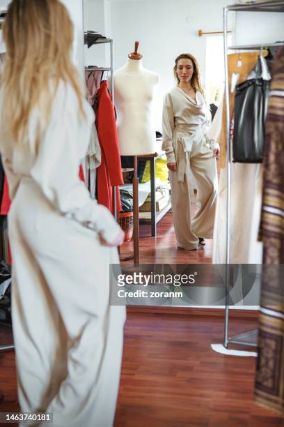 checking out her remodeled jumpsuit at the dressmaker's in front of the mirror - jumpsuit fashion stock pictures, royalty-free photos & images