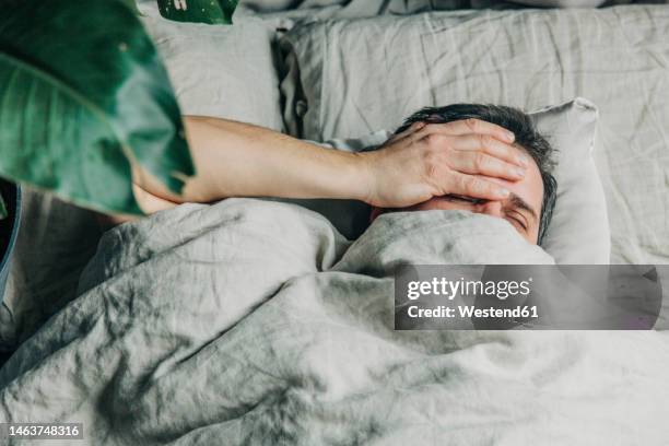 man with hand on head lying in bed - kopfschmerzen stock-fotos und bilder