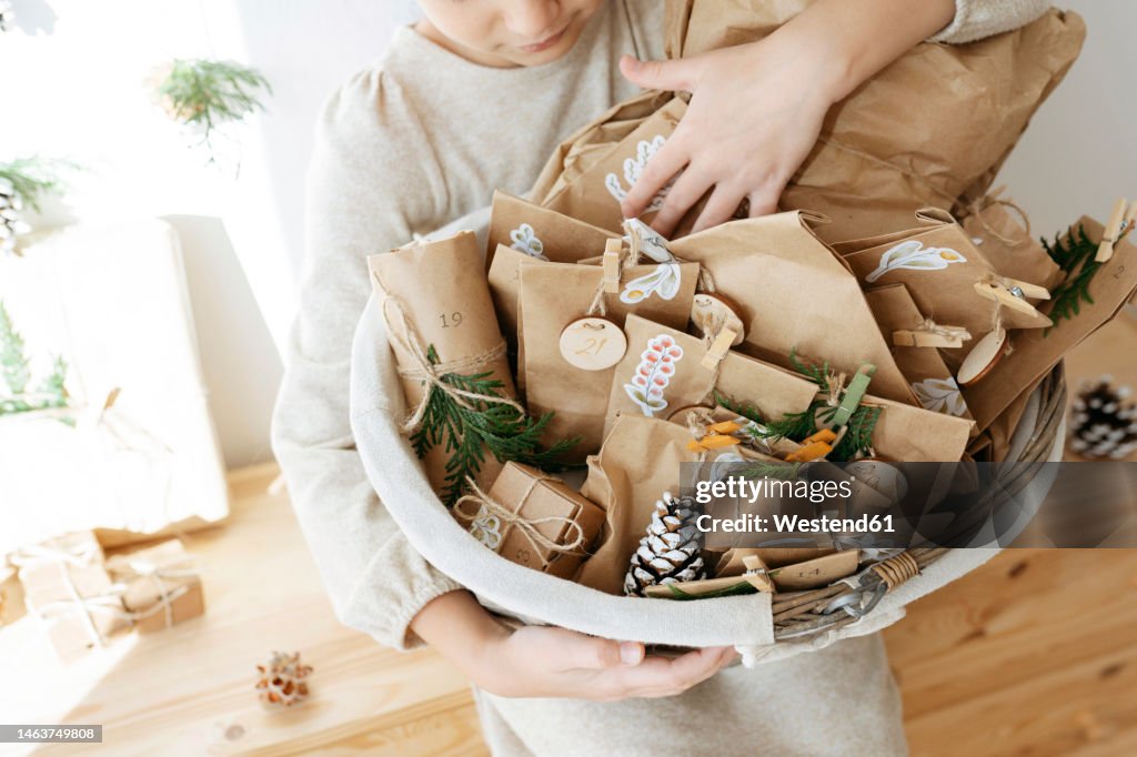Girl holding basket of advent calendar gifts at home