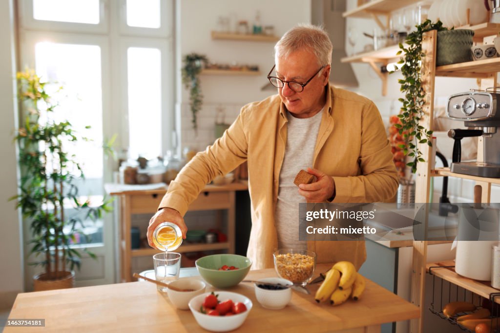 Uomo anziano che versa acqua nel bicchiere mentre fa colazione nella sua cucina domestica