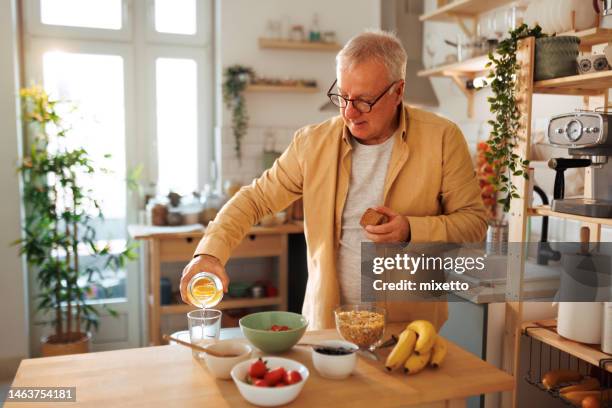 senior man pouring water in glass while having breakfast at his domestic kitchen - clean eating stock pictures, royalty-free photos & images