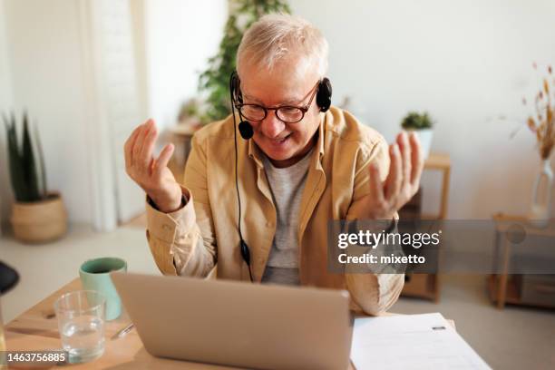 senior man with headset having video call at his apartment - office space movie stock pictures, royalty-free photos & images
